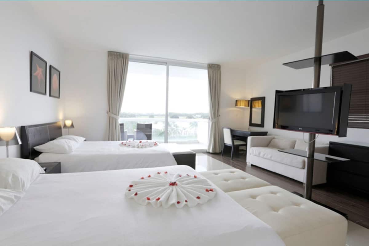 A hotel room with two beds, a television, a desk, and a view of the outdoors.