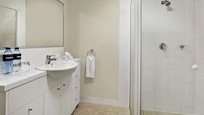 Un baño con lavabo, espejo y ducha. Hay botellas y una toalla en la encimera.