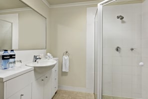 Un baño con lavabo, espejo y ducha. Hay botellas y una toalla en la encimera.