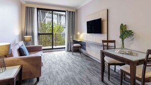 Una habitación de hotel moderna con sofá, una mesa de comedor, televisor montado en la pared y un balcón con cortinas.