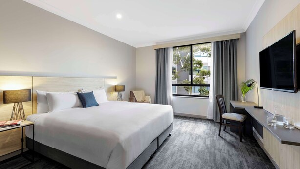 Habitación de hotel con una cama grande, un escritorio, una silla, un televisor y una ventana con cortinas.