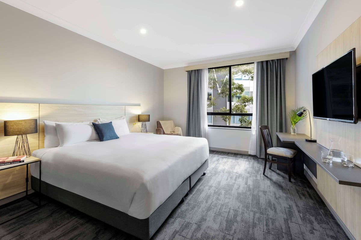 A hotel room with a large bed, a desk, a chair, a TV, and a window with curtains.