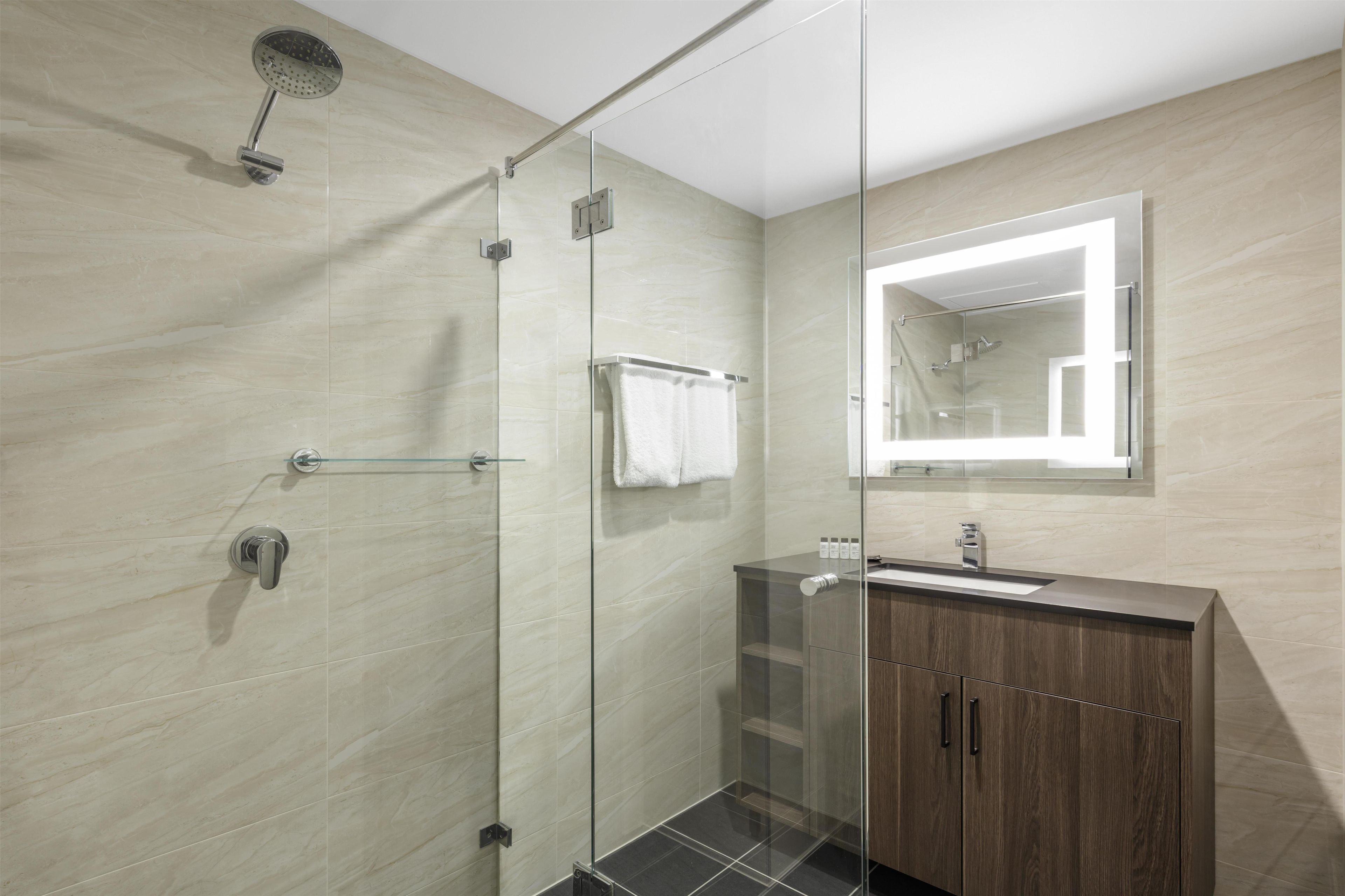 A modern bathroom with a glass-enclosed shower, a wooden vanity, and a mirror above the sink.