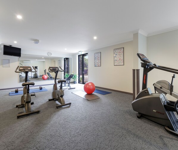 Un gimnasio con equipo de ejercicio, un espejo grande y una puerta que da al exterior.