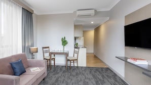 Una sala moderna con un sofá, una mesa de comedor con sillas, un televisor montado en la pared y un equipo de aire acondicionado.