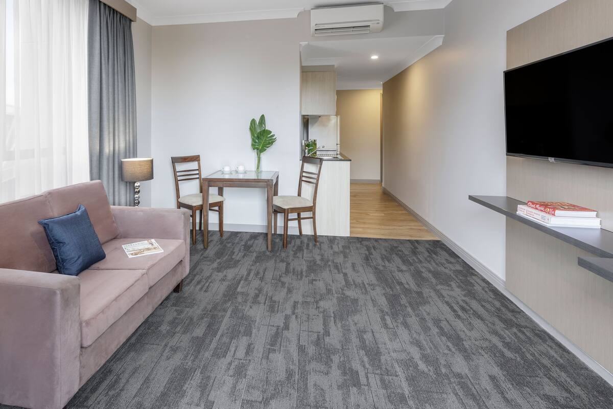 A modern living room with a sofa, a dining table with chairs, a TV mounted on the wall, and an air conditioning unit.