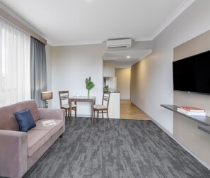 A modern living room with a sofa, a dining table with chairs, a TV mounted on the wall, and an air conditioning unit.