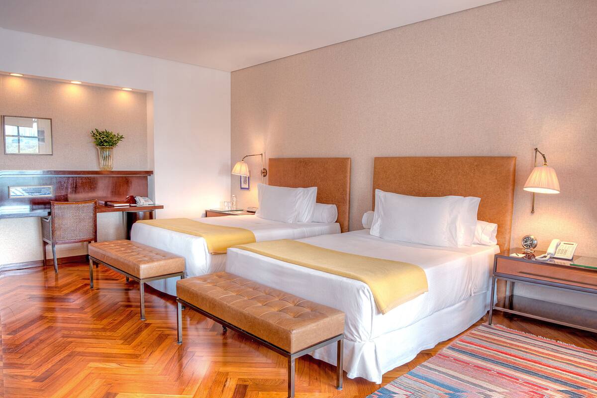 Habitación de hotel con dos camas, un banco, un escritorio y una silla.