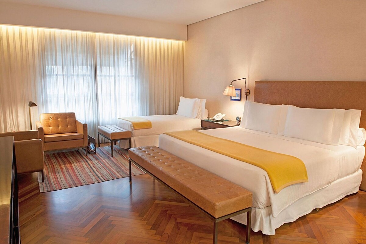 Een hotelkamer met een groot bed, een bank, een houten krukje, een bureau en een lamp.