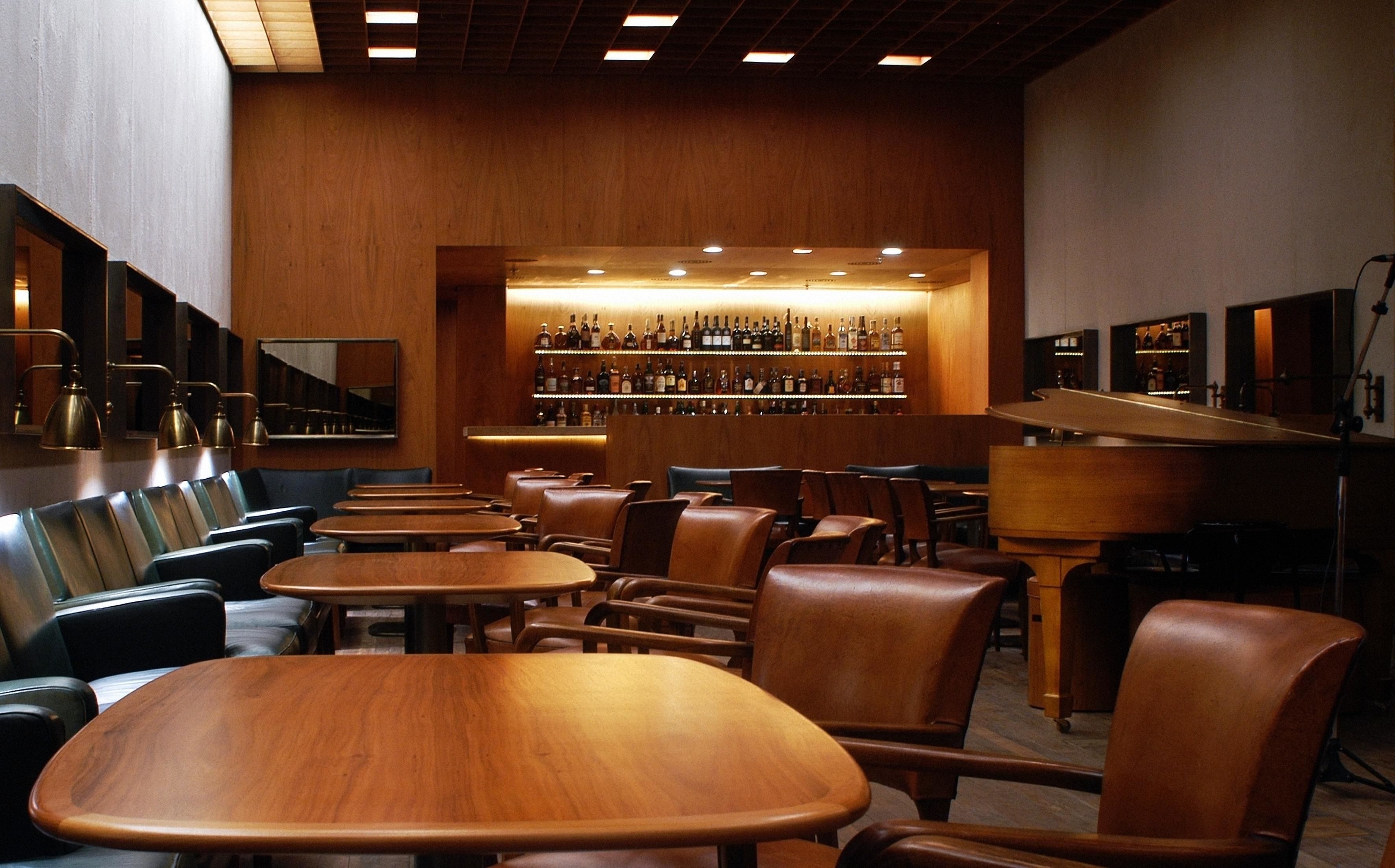 A bar area with wooden tables and chairs, a wall of liquor bottles, and a mirrored wall.