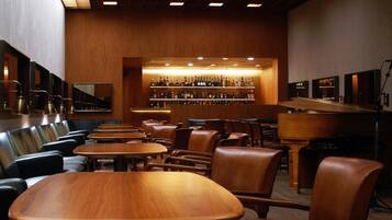 A bar area with wooden tables and chairs, a wall of liquor bottles, and a mirrored wall.