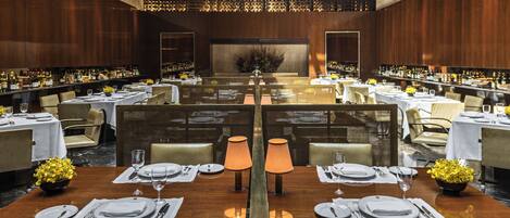 A spacious dining area with multiple tables set for service, a central decorative wall, and a high ceiling.