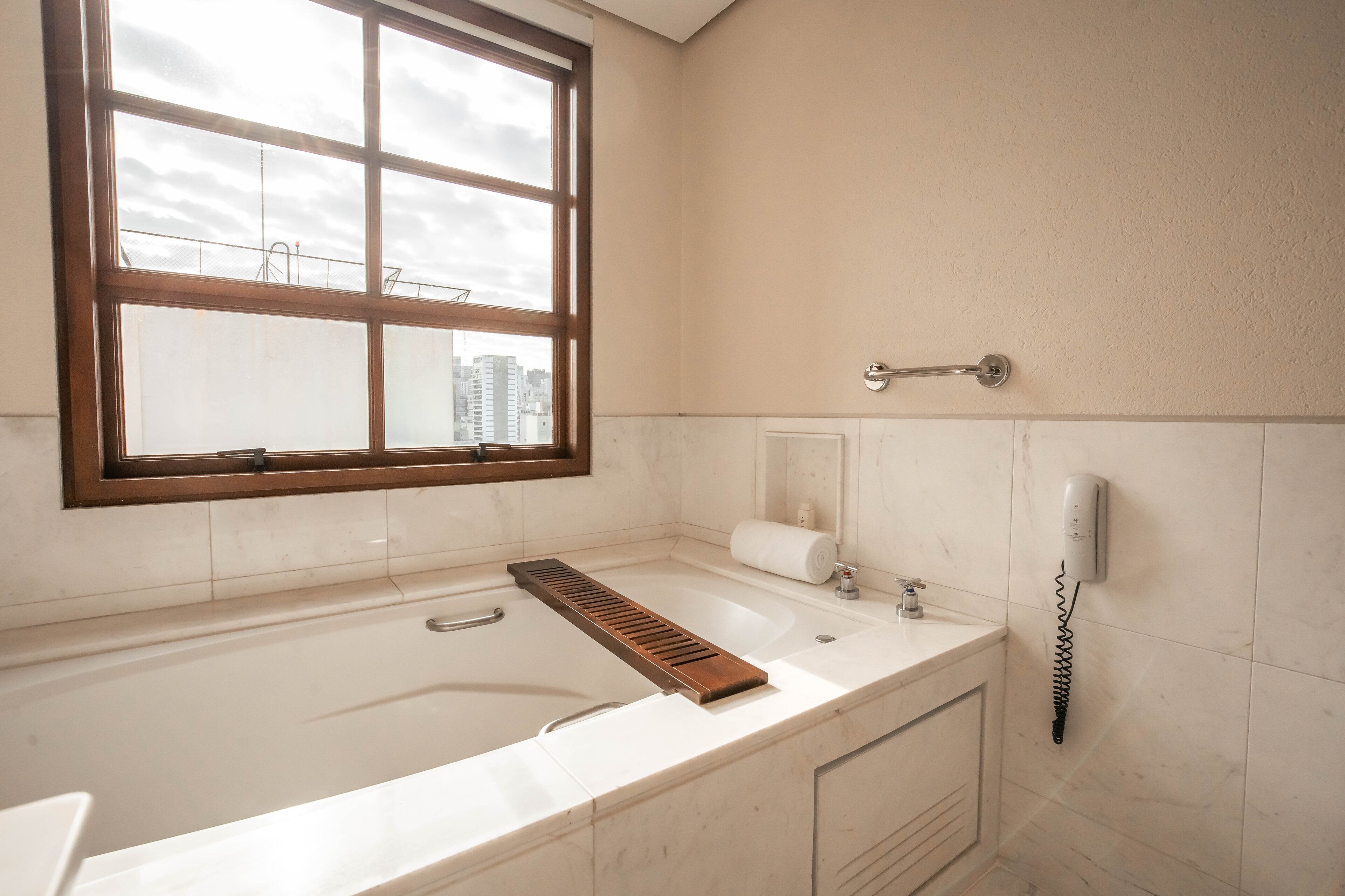 A bathroom with a large bathtub, a window, a towel dispenser, and a hand dryer.