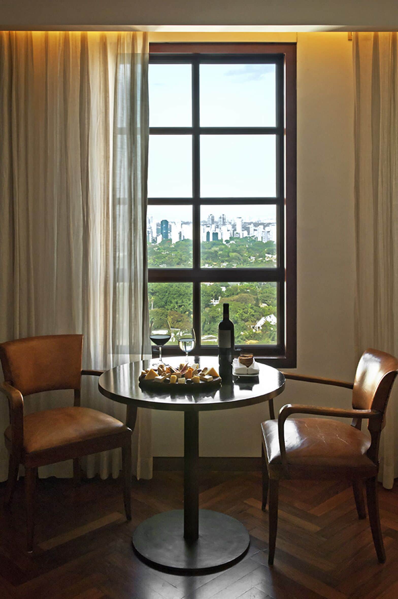 A room with a table and two chairs, a window with a city view, and a bottle on the table.