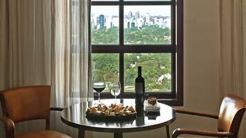 A room with a table and two chairs, a window with a city view, and a bottle on the table.