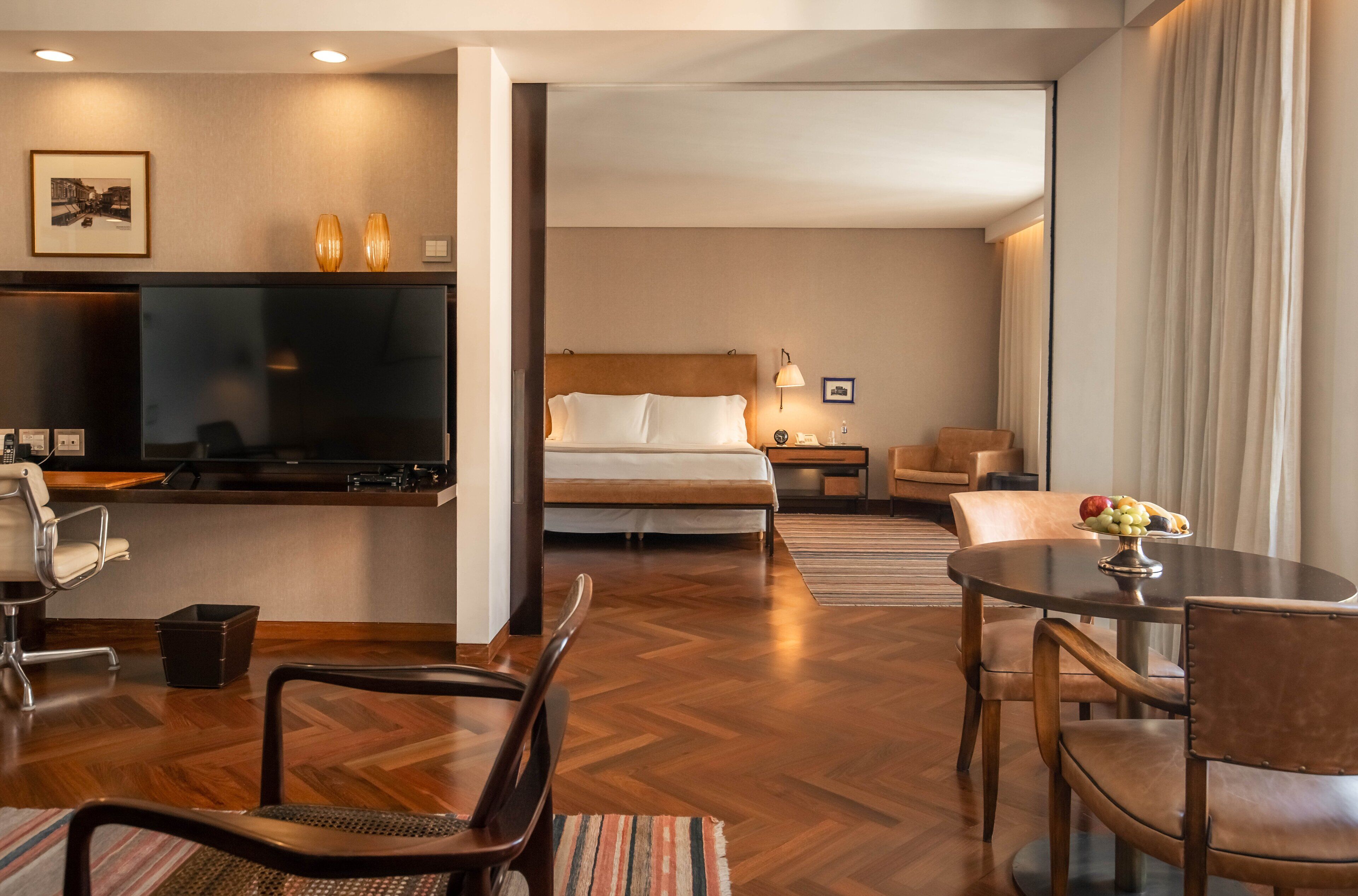 Een hotelkamer met een bed, een bureau, een stoel, een televisie en een eettafel met fruit.