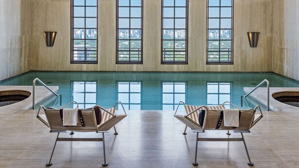 Zona de piscina con dos sillones de descanso y amplios ventanales con vistas a la ciudad.