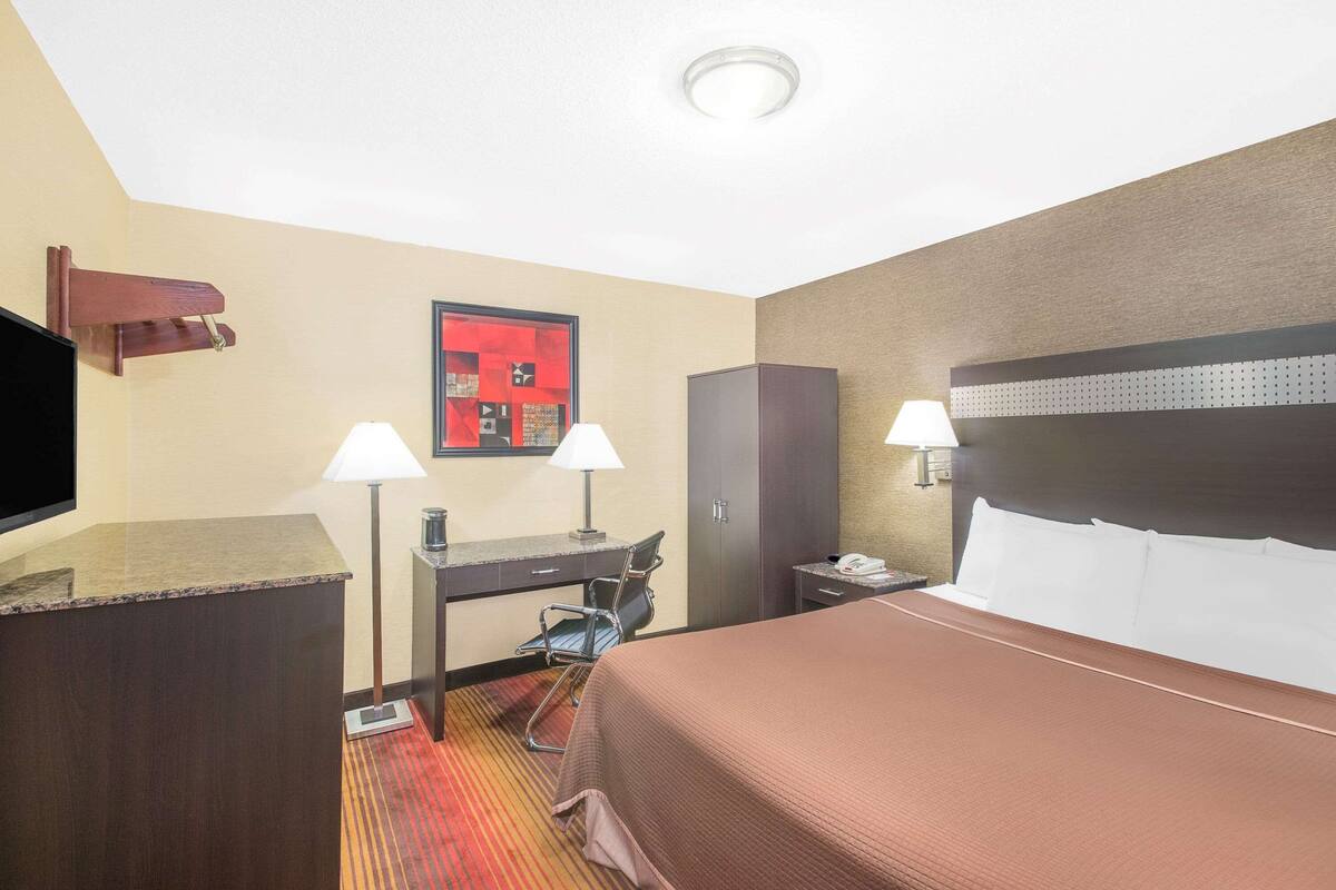 Ein Hotelzimmer mit Bett, Schreibtisch, Stuhl, Fernseher und zwei Lampen.
