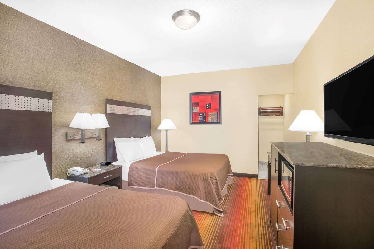 Ein Hotelzimmer mit zwei Betten, einem Fernseher, einem Schreibtisch und einem Spiegel.