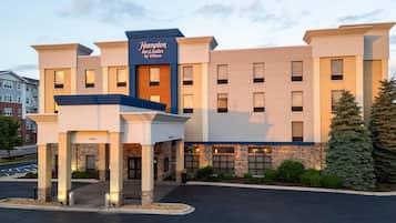 A Hampton Inn & Suites by Hilton hotel with a modern design, featuring a prominent entrance and a parking lot.