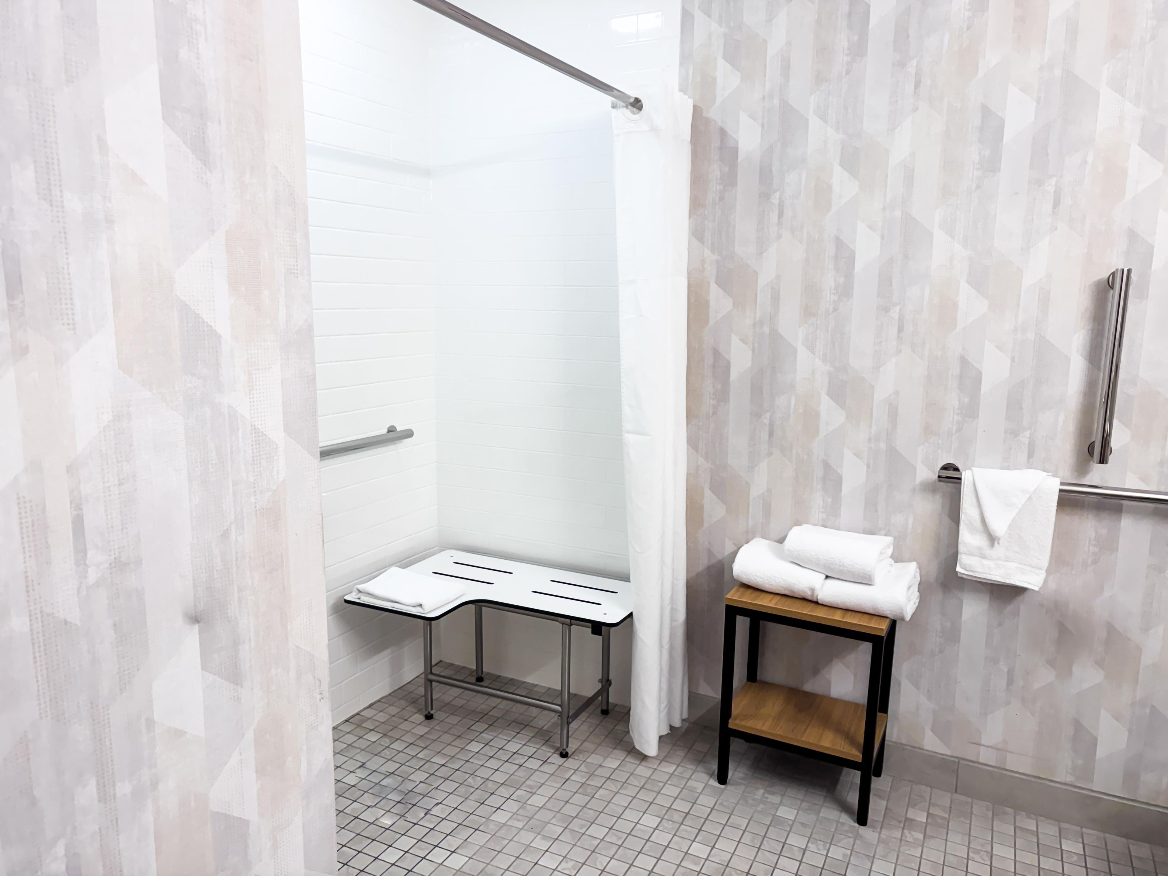 A modern bathroom with a shower, a towel rack, and a small table.