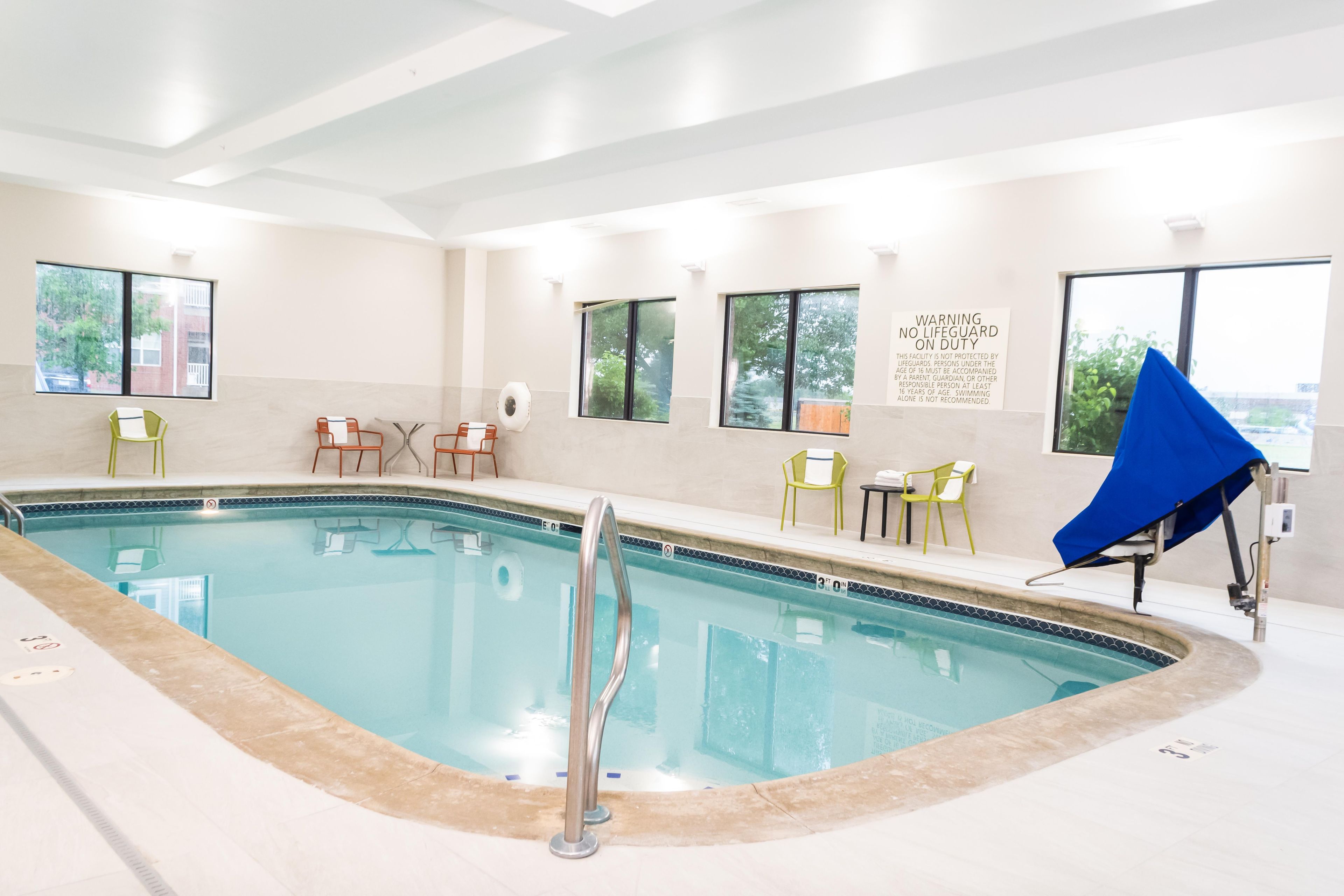 A swimming pool with a lifeguard chair, lounge chairs, and a warning sign.