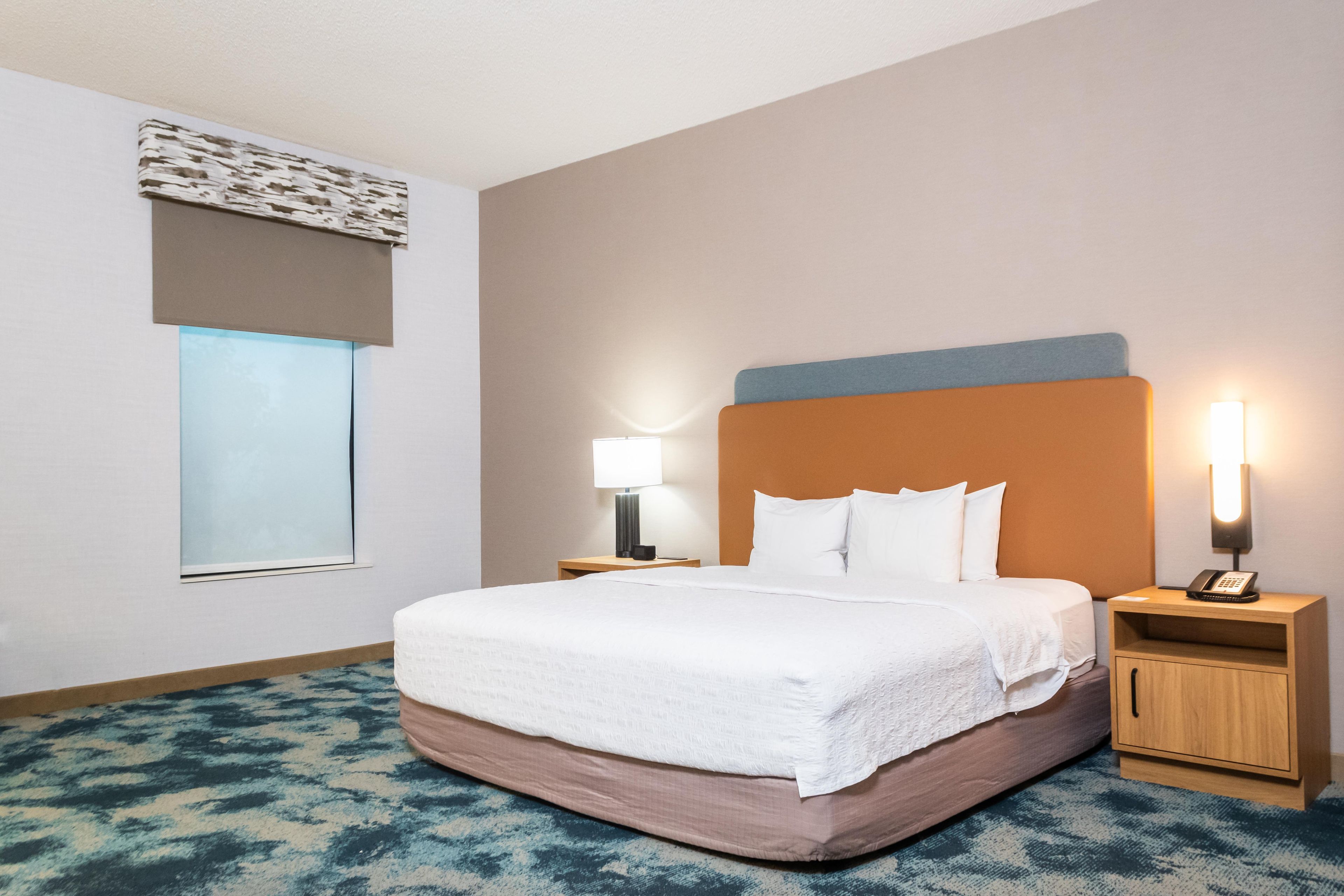 Quarto de hotel com cama grande, duas mesas de cabeceira, uma janela e luminária fixada na parede.