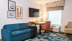 A room with a blue sofa, a small round table, a red chair, a television mounted on the wall, and framed pictures.
