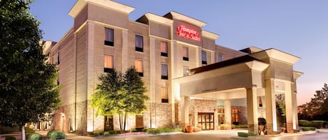 Un hotel Hampton Inn & Suites con fachada de ladrillo, múltiples ventanas y un área de entrada bien iluminada.