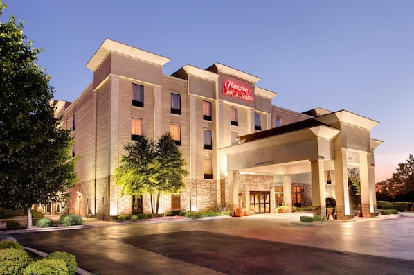 Un hotel Hampton Inn & Suites con fachada de ladrillo, múltiples ventanas y un área de entrada bien iluminada.
