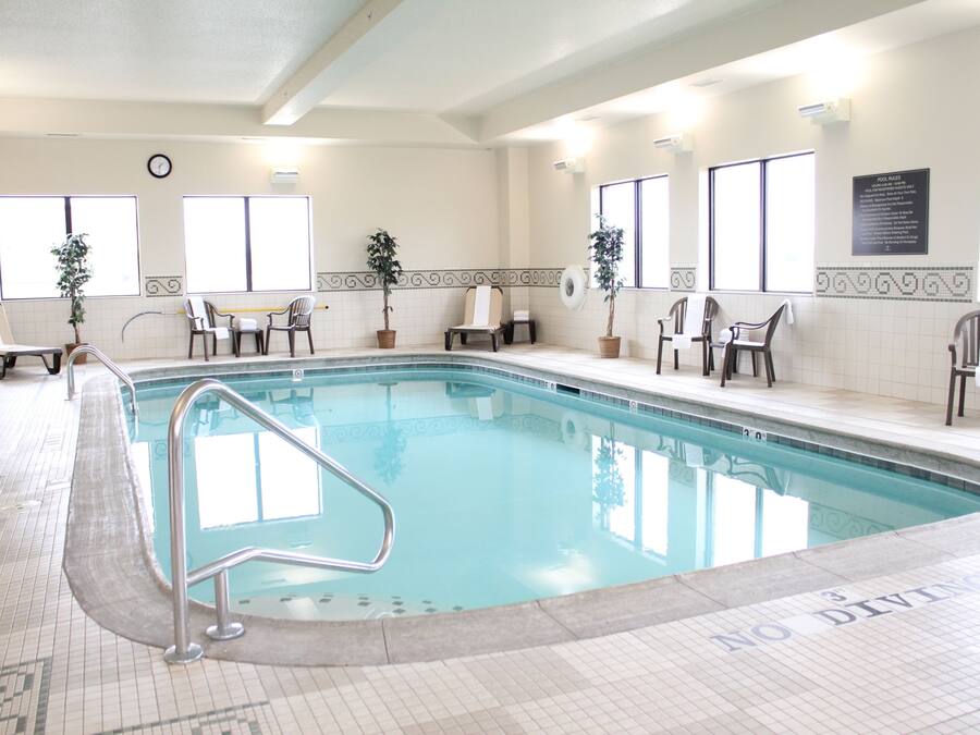 An indoor swimming pool with a no diving sign, chairs, potted plants, and a clock on the wall.