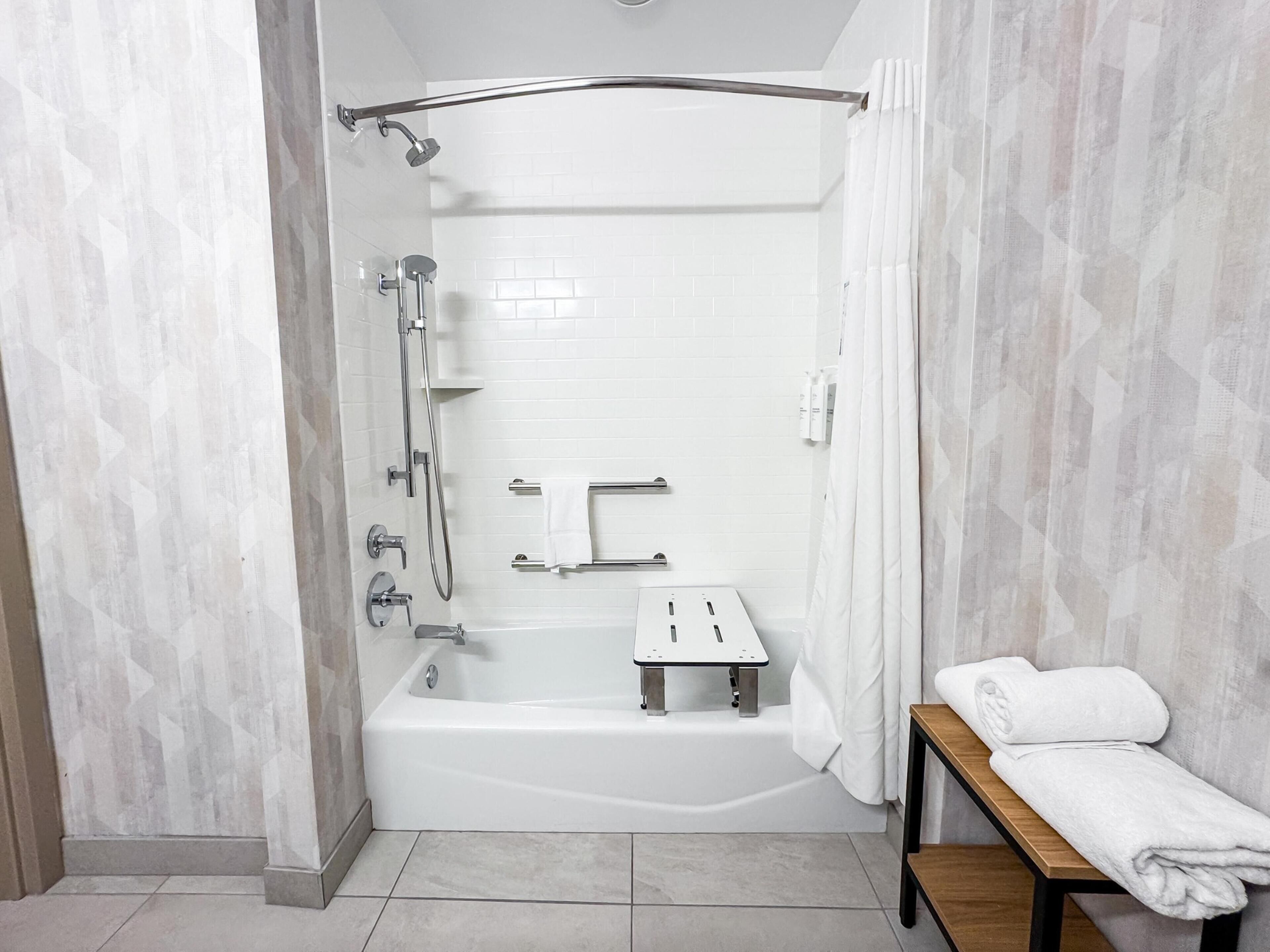 A modern bathroom with a bathtub, shower, and a bench with towels.