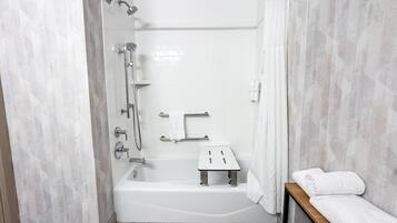 A modern bathroom with a bathtub, shower, and a bench with towels.