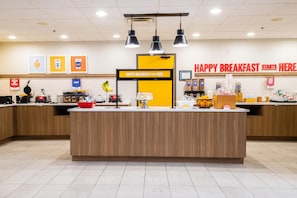 Mostrador de desayuno con un letrero que dice 'HAPPY BREAKFAST STARTS HERE' y diversos alimentos y condimentos disponibles para la venta.