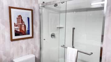 A modern bathroom with a glass-enclosed shower, a white toilet, and a framed picture on the wall.