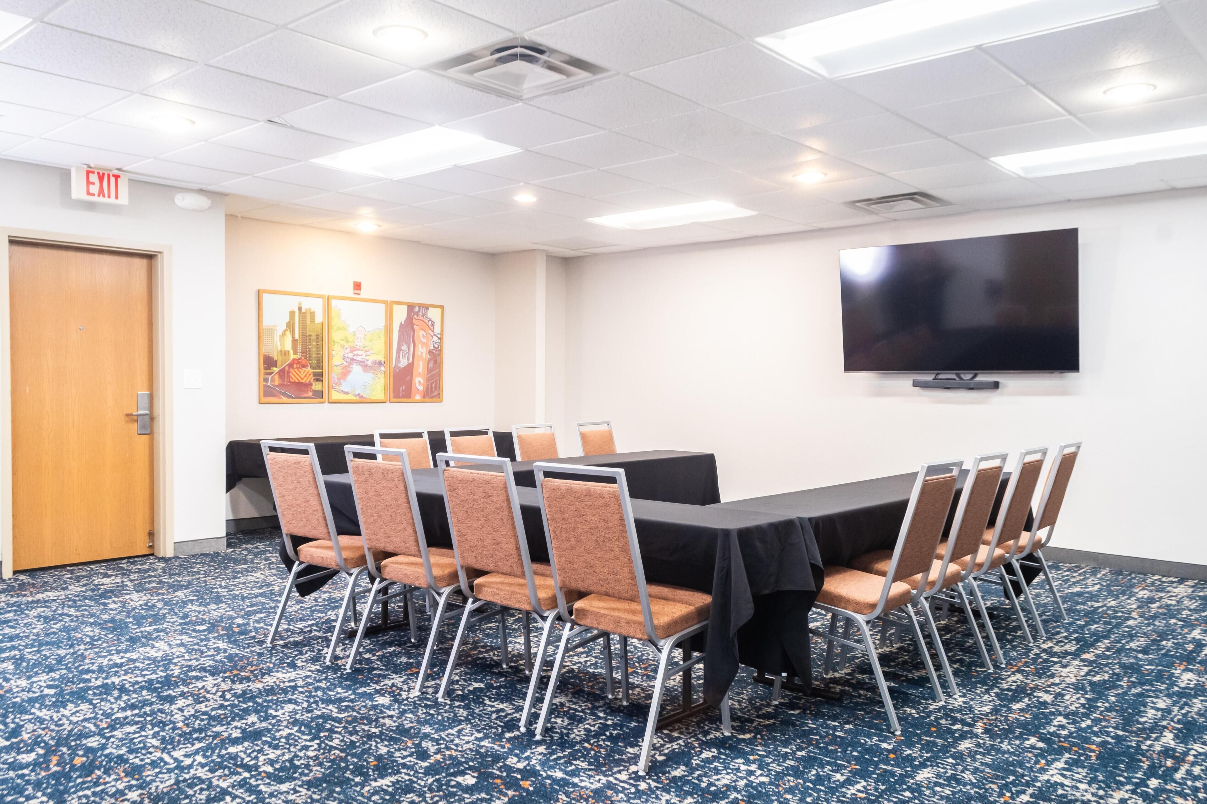 Une salle de conférence équipée d’une grande table, de chaises, d’un téléviseur à écran plat et d’un panneau indiquant la sortie.