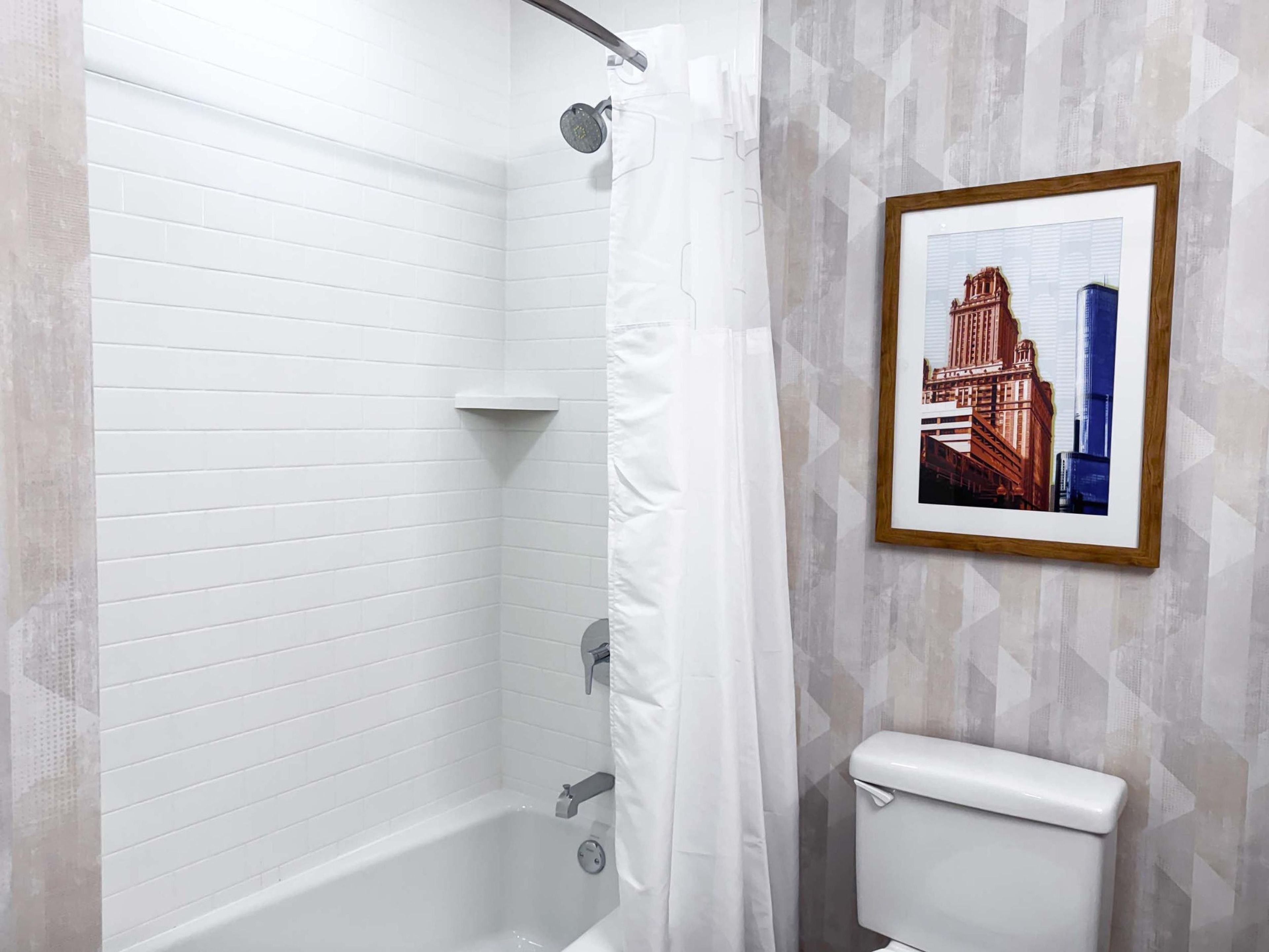 Une salle de bain avec une baignoire blanche, un rideau de douche et des toilettes. Un tableau encadré représentant un bâtiment est accroché au mur.