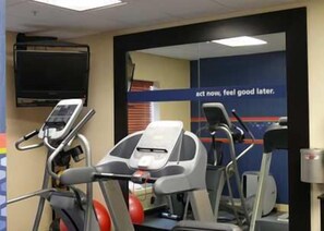 Et fitnessrum med løbebånd, træningsbolde, et fjernsyn og motiverende tekst på væggen.