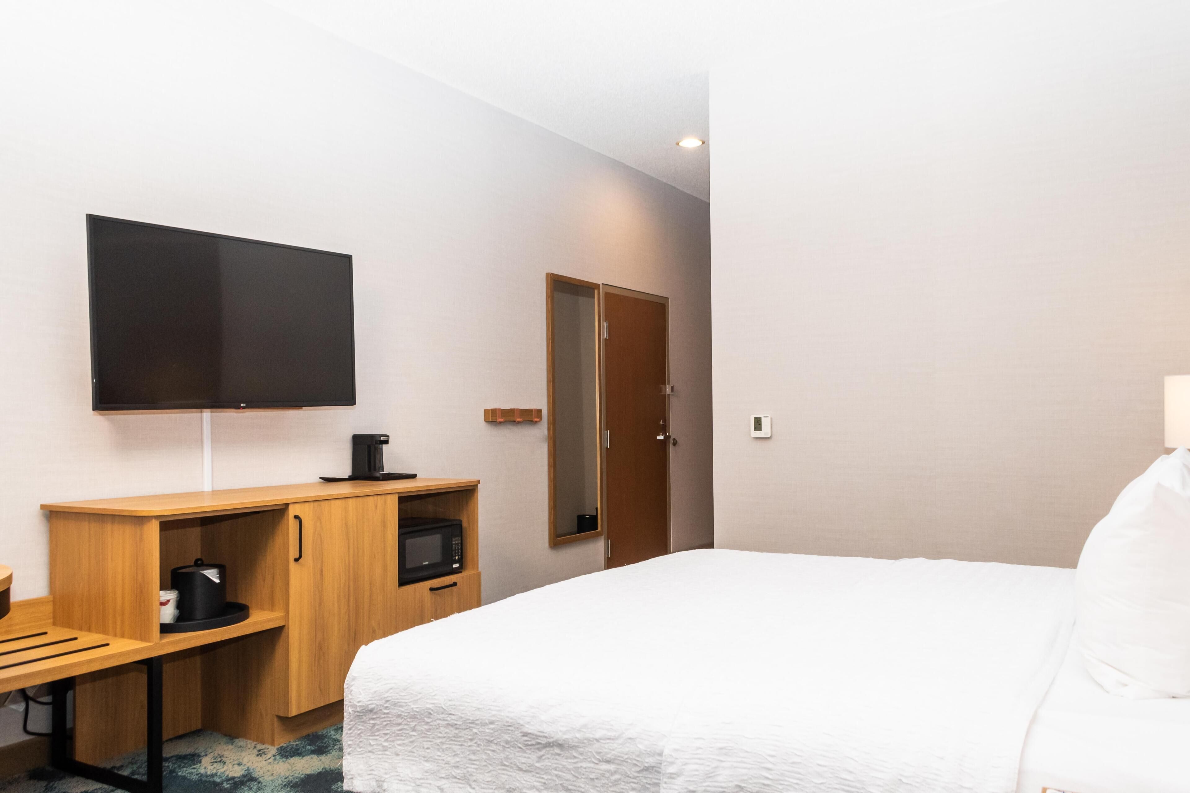 A hotel room with a bed, a desk with a coffee maker, a television, and a door.