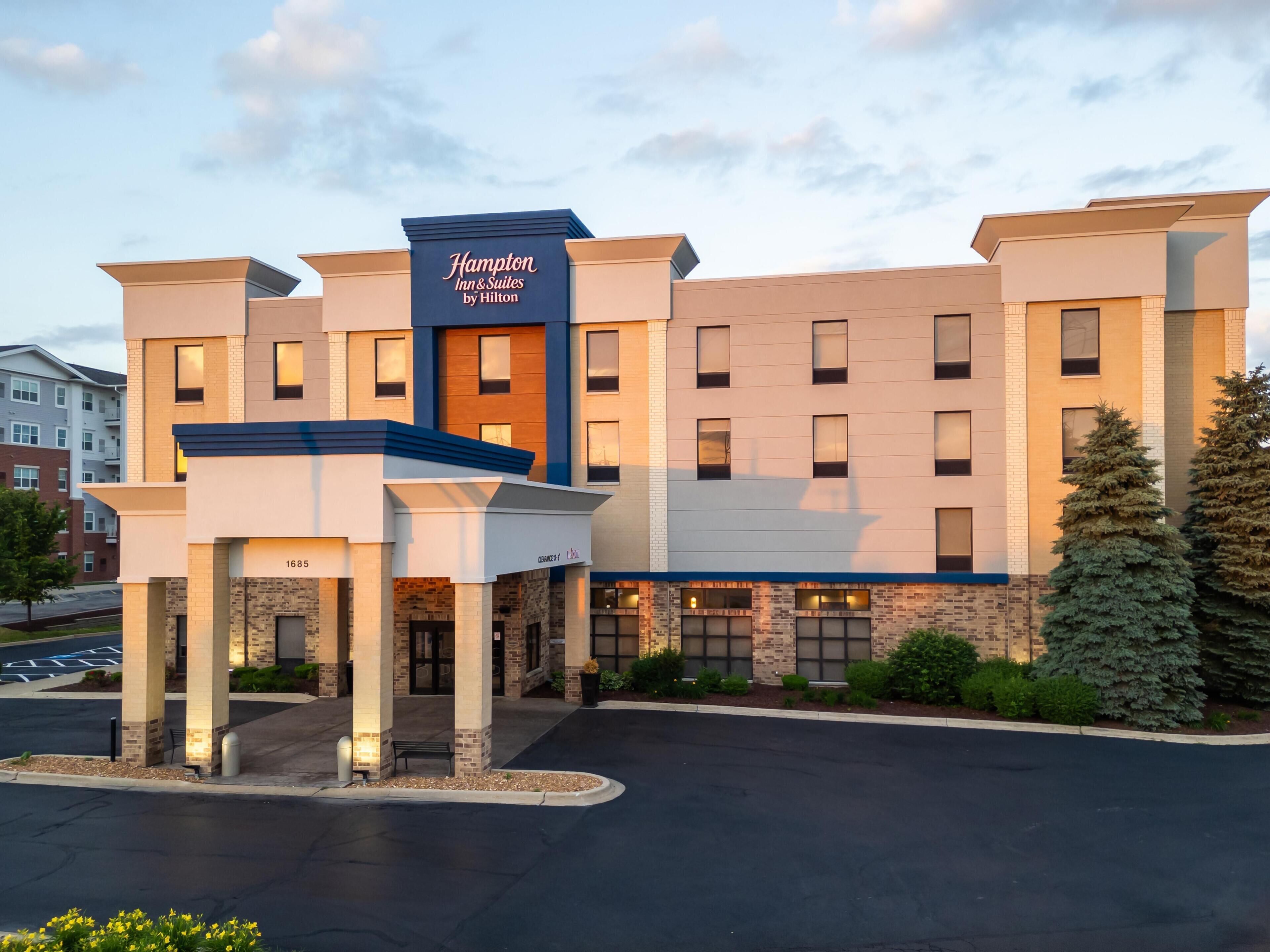 Un hotel Hampton Inn & Suites by Hilton con un diseño moderno, que cuenta con una entrada destacada y un estacionamiento.