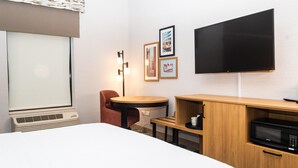 A hotel room with a bed, a desk, a chair, a flat-screen TV, and a microwave.