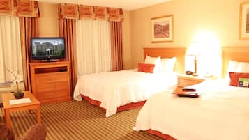 A hotel room with two beds, a television, a desk with a lamp, and a painting on the wall.