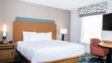A hotel room with a bed, bedside tables, a desk, a chair, a lamp, and a TV.