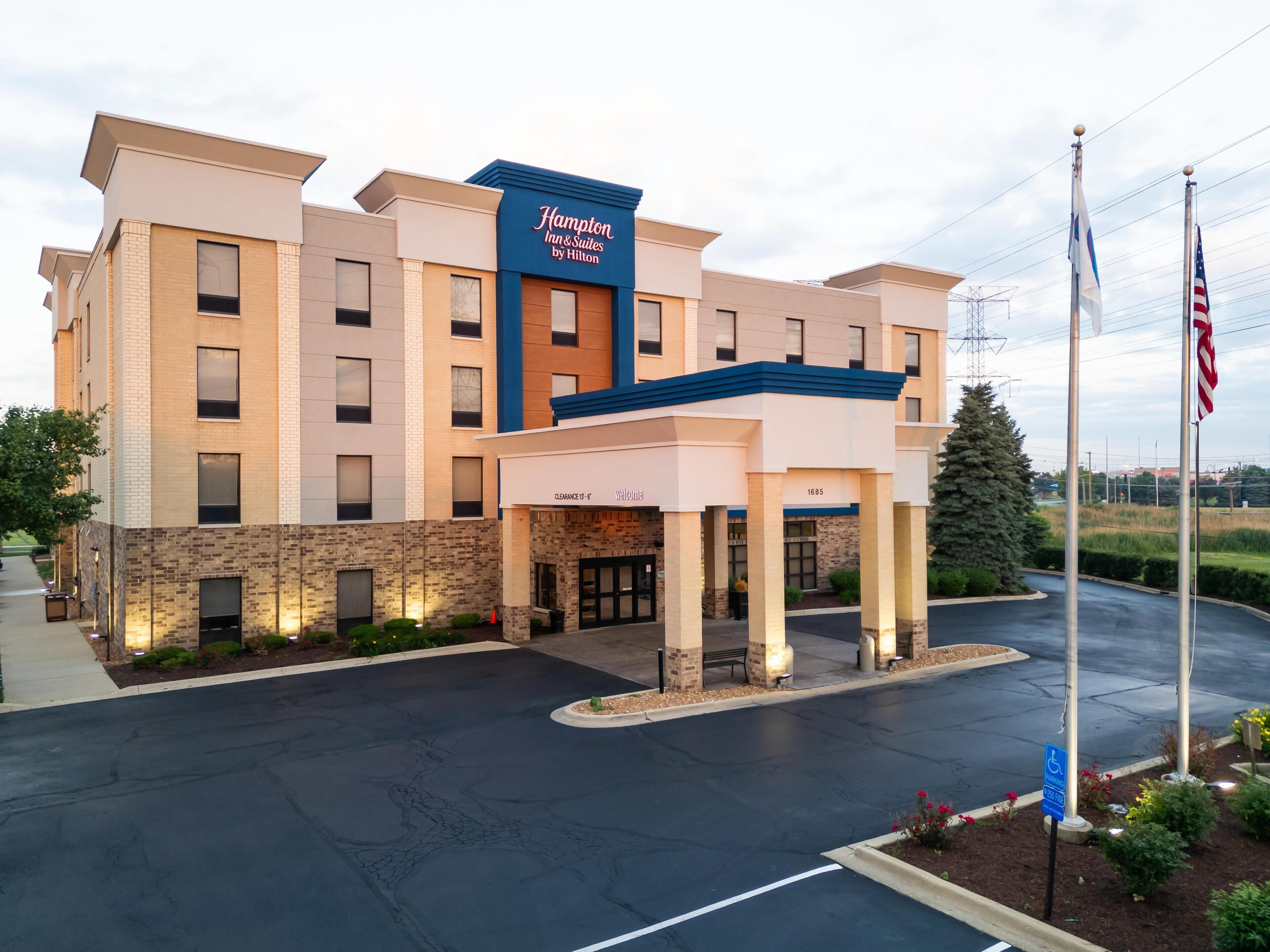 Un hôtel Hampton Inn & Suites de la chaîne Hilton, avec une façade en briques, une entrée abritée et un parking.