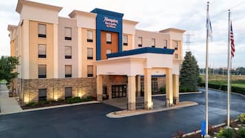 Un hôtel Hampton Inn & Suites de la chaîne Hilton, avec une façade en briques, une entrée abritée et un parking.