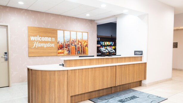A reception desk with a 'Welcome to Hampton' sign, a cityscape artwork, and a 'Hilton Honors' plaque.