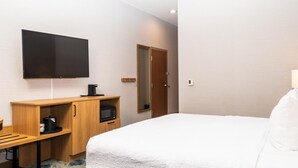 A hotel room with a bed, a desk with a coffee maker, a television, and a door.