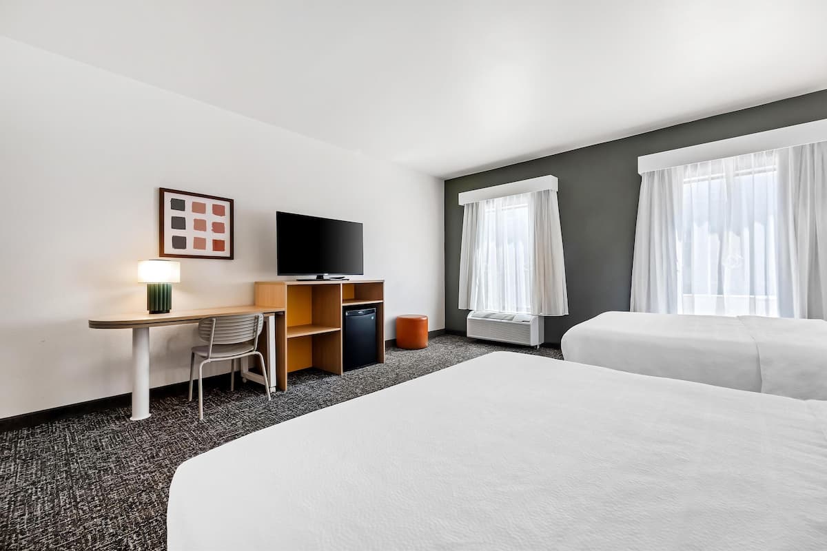 Hotellihuone, jossa on sänky, työpöytä tuolilla, televisio ja ikkuna, jossa on verhot.