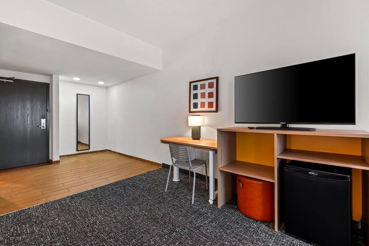 Moderni hotellihuone, jossa on työpöytä, tuoli, televisio ja säilytystilaa.