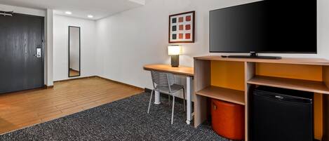 Quarto de hotel moderno com escrivaninha, cadeira, televisão e unidade de armazenamento.